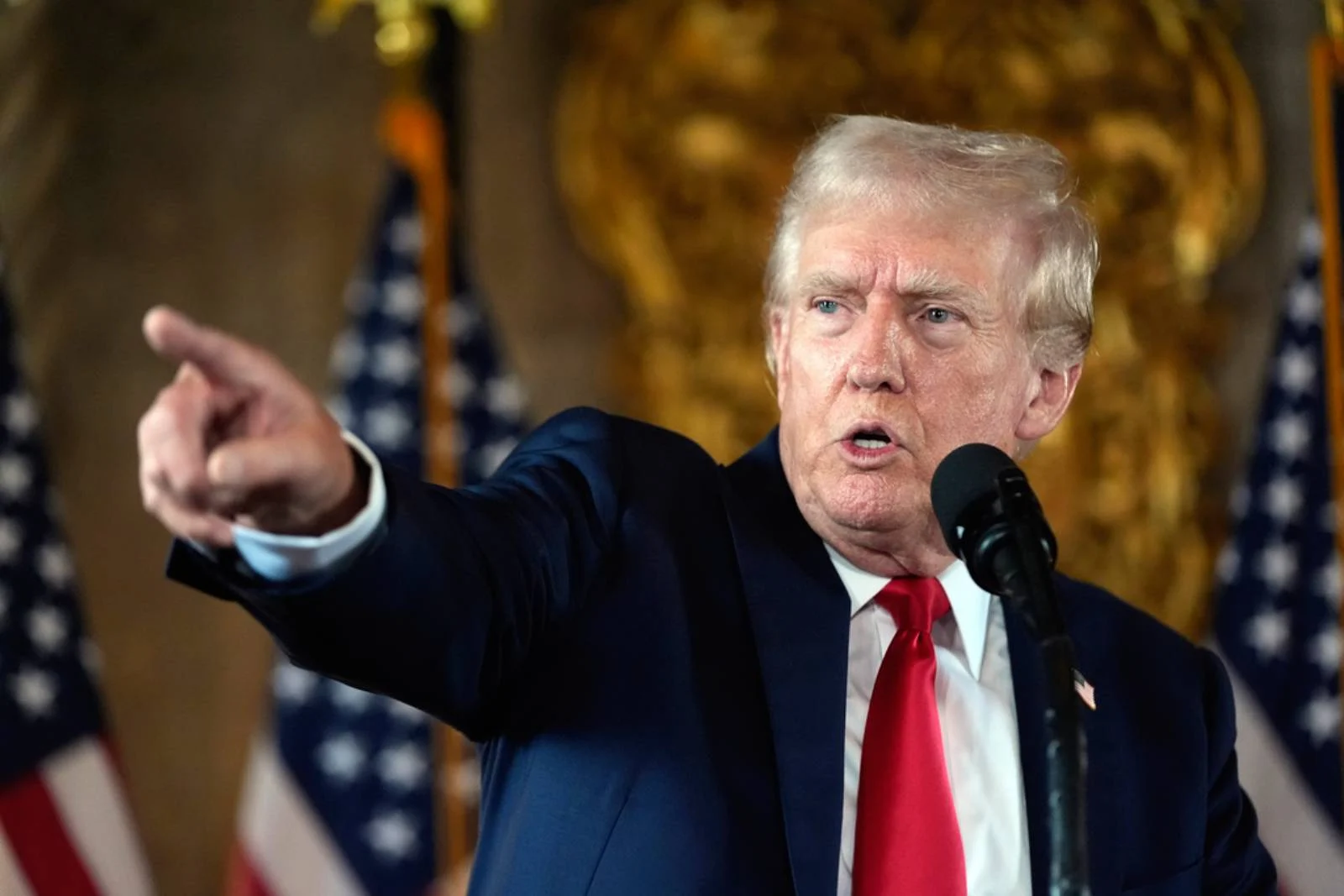 US President Donald Trump standing in front of 3 American flags giving a speech